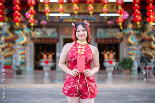 Portrait smiles Asian young woman wearing red cheongsam dress holding red envelopes decoration for Chinese new year festival celebrate culture of china at Chinese shrine Public places in Thailand