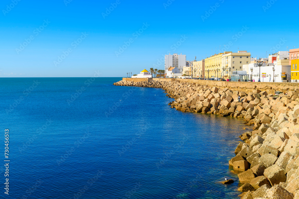 View from the rocky coastline and breakwater along Campo del Sur of the cityscape, Mediterranean Sea and historic town of Cadiz Spain.	