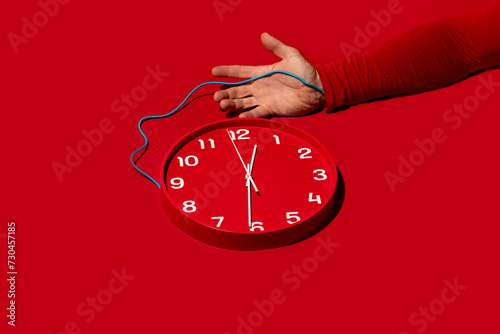 Conceptual image of arm wired to clock on red background photo