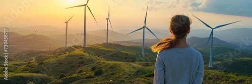 Woman overlooking wind farm with windmill turbine power generators in a hilly outdoor landscape