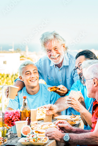 Multigenerational family having lunch on a terrace on a beautiful sunny day. 18 year old boy laughs with his grandparents celebrating. Lifestyle and family concept.   