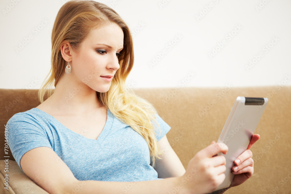 A woman on a sofa reading from a digital tablet