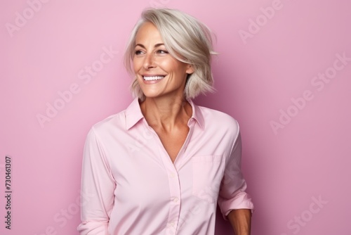 Portrait of a smiling mature woman in pink shirt on pink background © Loli