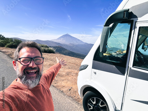 One adult man taking selfie picture outside a camper van motorhome parking in the mountain scenic view background. People and travel alternative lifestyle vanlife vacation renting vehicle. Leisure