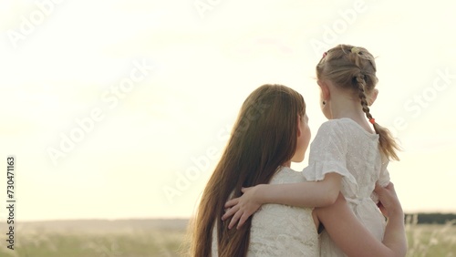 Carefree childhood, happy daughter hugs mother outdoors. Child, girl hugging her mother in summer park in sun. Happy family on walk in field looking to future. Mom, child play together on sunny day