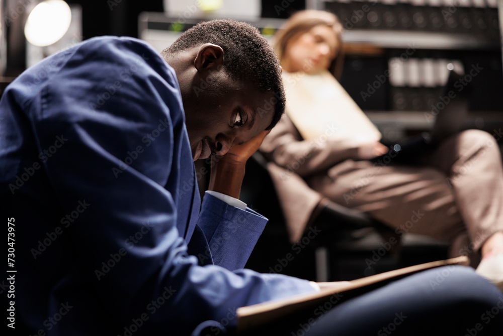Tired private inspectors checking files with crime scene evidence, discovering confidential report in arhive room. Overworked diverse detectives working late at night at missing person case Tired private inspectors checking files with crime scene evidence, discovering confidential report in arhive room. Overworked diverse detectives working late at night at missing person case