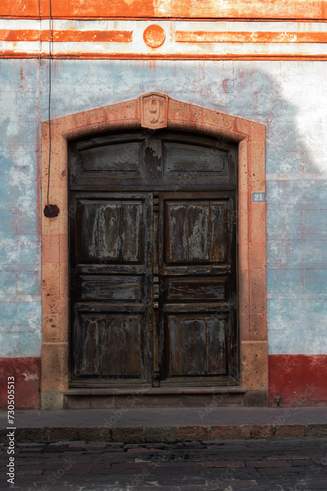 old wooden door of a house with a blue facade with red stripes in the center of a historic city with number nine on the top of the door and with number twenty one to the side of the door 