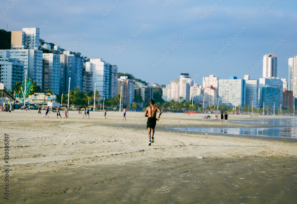 Man running on the beach. In the background buildings and bathers. Man running on the beach. In the background buildings and bathers.