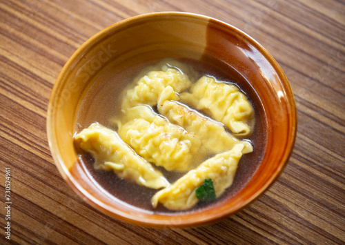 Chinese dumpling soup in a bowl on a wooden table.
