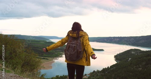 Back of woman, hiking and arms up with nature, journey and mountain top with view or energy. Person, hiker or girl with backpack or winner with environment, travel or health with adventure or explore photo