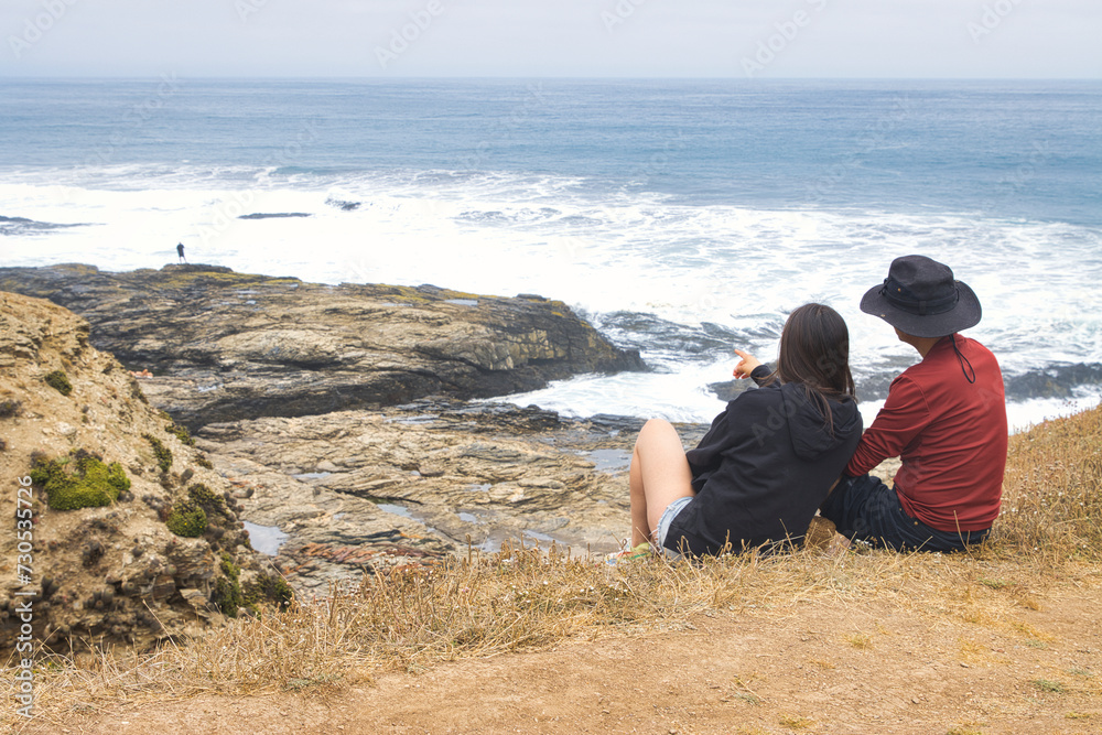 Pareja de turistas disfruta del borde de la costa, conversa ríe, observa la naturaleza.