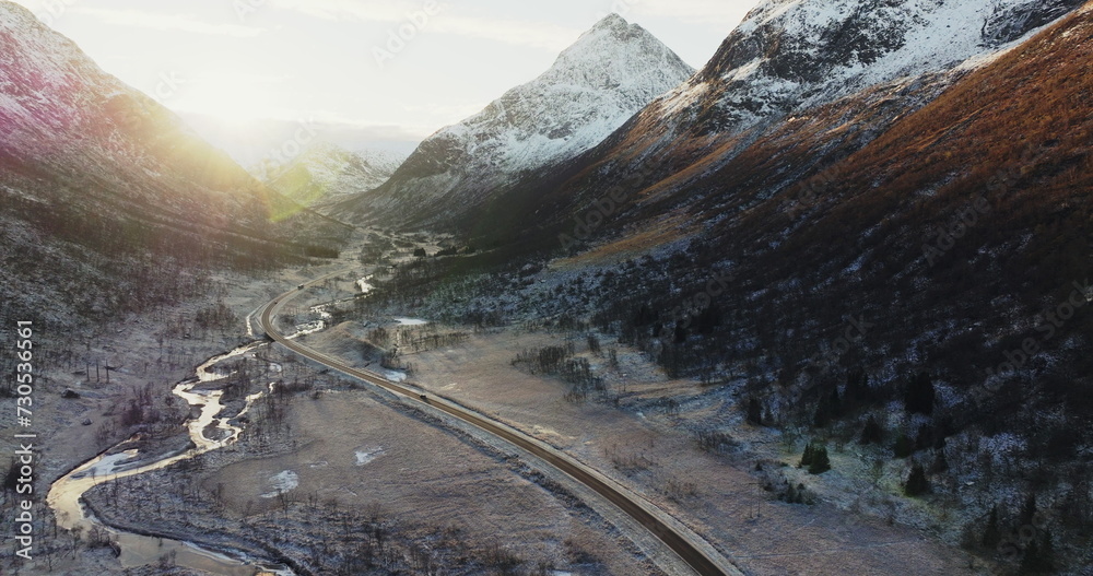 Sunlit Peaks and Winding River: Aerial View of a Norwegian Valley. E10 Road Through Snowy Peaks: Aerial View of Lofoten's Winter Landscape