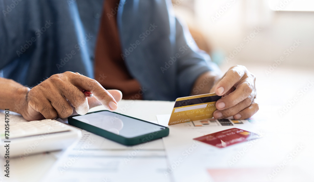 Man calculate expenses from credit card at home. home shopping concept via credit card and use mobile banking app to pay Man calculate expenses from credit card at home. home shopping concept via credit card and use mobile banking app to pay