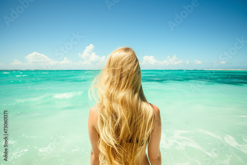 young blonde woman walks into turquoise sea water  rear view