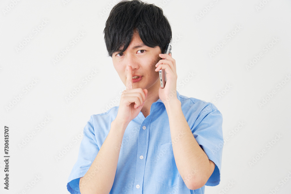 秘密のジェスチャーをしながらスマートフォンで電話する男性 白背景 秘密のジェスチャーをしながらスマートフォンで電話する男性 白背景