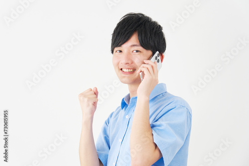 ガッツポーズをしながらスマートフォンで電話する男性 白背景