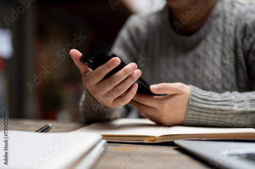  Close-up image of a woman using her smartphone while working at her desk.