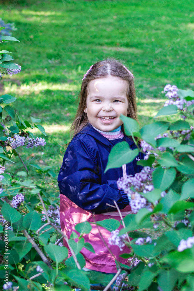Adorable smiling little girl in a garden with lilac trees. Candid child portrait at spring season. Adorable smiling little girl in a garden with lilac trees. Candid child portrait at spring season.