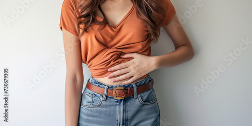 Indoor shot of displeased woman suffering from painful period cramps, holds hands on belly, has pain in stomach, stomachache, upset expression, wears long sleeve shirt on studio background photo