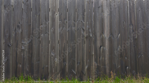 brown planks wooden background of fence wall of vertical wood boards on a horizontal facade with floor grass