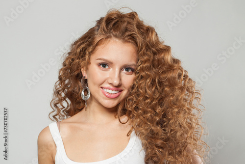Friendly redhead female model with long frizzy ginger hair and clean soft fresh skin posing on white background. Studio fashion beauty portrait of young woman
