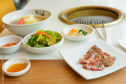 Japanese yakiniku (grilled meat) served alongside a bowl of refreshing cold noodles. The yakiniku features tender, perfectly grilled slices of meat with a caramelized glaze