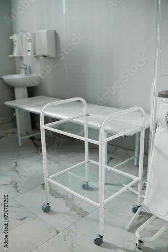 Empty push cart standing in front of camera against other medical equipment standing by wall of spacious ward or office