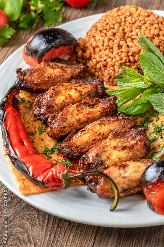 Barbecue chicken wings garnished with bulgur pilaf, roasted peppers and tomatoes. Traditional Turkish chicken wings