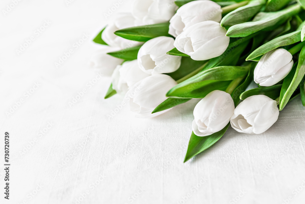 fresh bouquet of white tulips with lush green leaves on white textured surface, Mothers day or Women's day. Top view with copy space Floral composition Romantic background