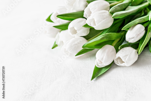 fresh bouquet of white tulips with lush green leaves on white textured surface, Mothers day or Women's day. Top view with copy space Floral composition Romantic background