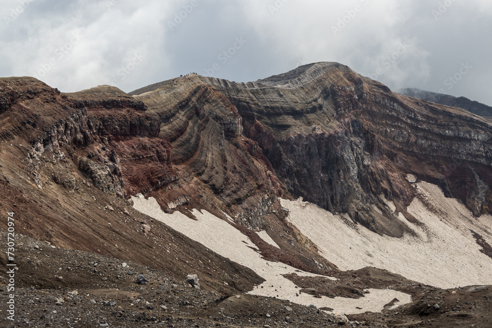 Majestic mountain landscape. The rim of a volcanic crater. View of the rock layers on the inner slope of the volcano's crater. Nature of the Russian Far East. Gorely volcano, Kamchatka Krai, Russia.