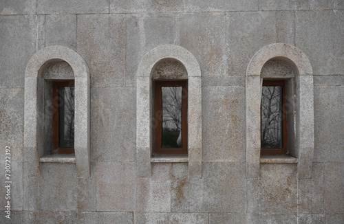 3 three arched Classic windows in granite exterior wall. small wooden arched windows protected. windows set into a solid wall built of granite blocks, in front. orthodox church in Georgia.