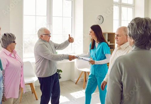 Nurse meets with elderly patients in retirement home. Old man shakes hands with happy young nurse, gives her thumbs up and says that he likes it here. Senior care concept