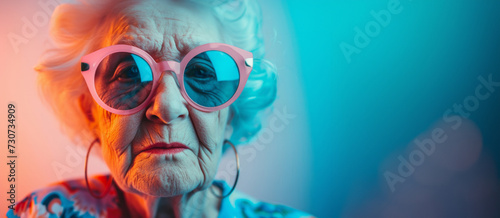 Portrait of good looking senior woman wears spectacles bright makeup looks at camera with pleased expressionisolated over colorful background. People age concept. Image of a beautiful and elegant old 