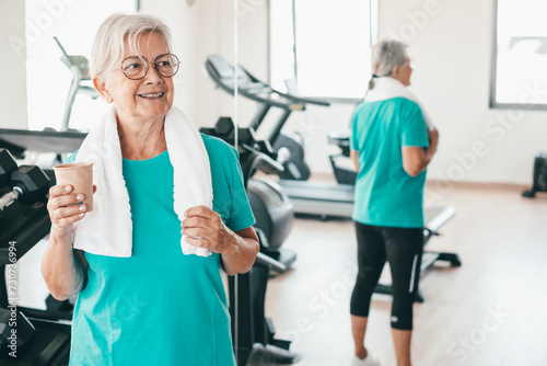 Smiling and active retired senior woman in gym area takes a break from exercises drinking. Sport  health  gym  wellness concept