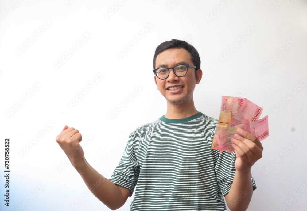 an asian adult man smiling while holding paper money or bank note with happy expression an asian adult man smiling while holding paper money or bank note with happy expression