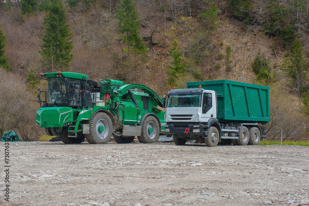 Fototapeta premium An industrial wood chipper with off-road capability and a truck on a logging site near the mountain village of Forni Avoltri in Carnia, Udine Province, Friuli-Venezia Giulia, north east Italy