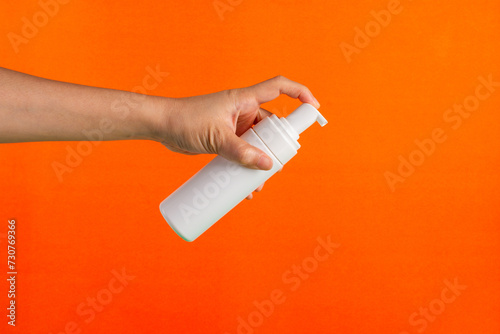 Cosmetic white bottle. Womens cosmetic accessory and hand for makeup on orange background.