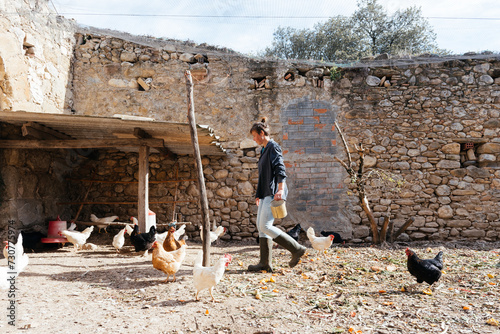 Woman feeding chickens while walking in paddock with chickens and feeding