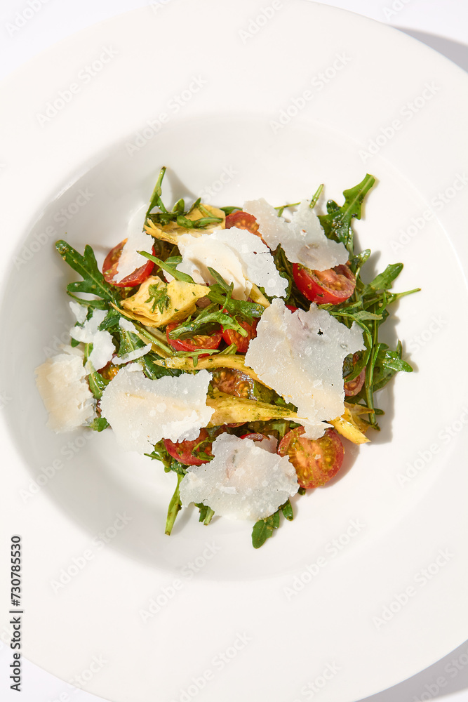 Top view of a salad with artichokes, tomatoes, and shaved Parmesan cheese on a white plate Top view of a salad with artichokes, tomatoes, and shaved Parmesan cheese on a white plate