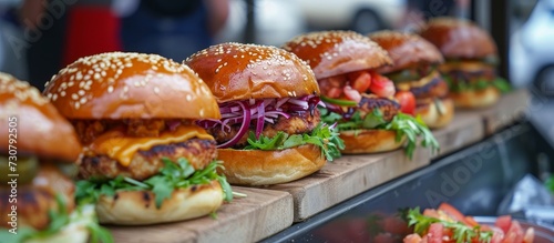 A wooden cutting board holds a row of hamburgers, a staple food in fast food culture, made with ingredients like buns and produce.