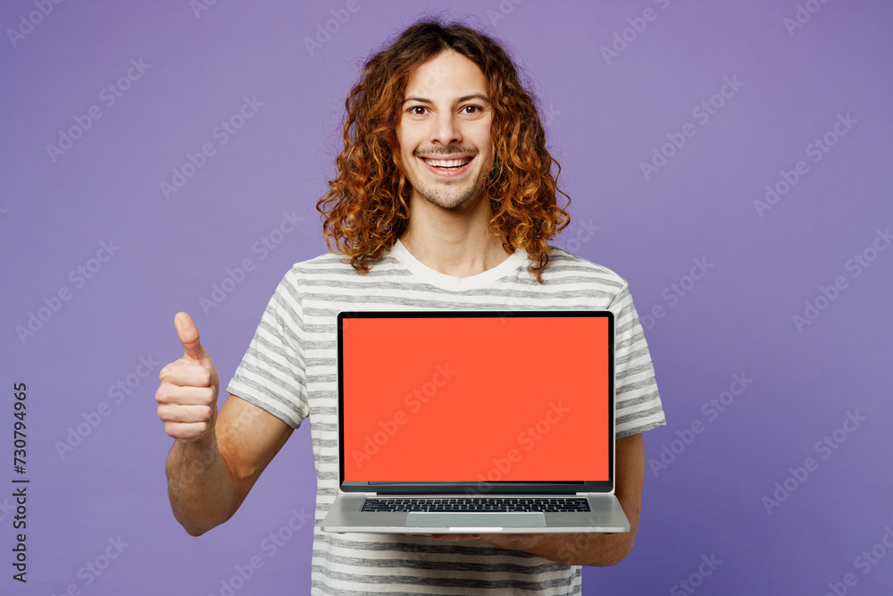 Young IT man wear grey striped t-shirt casual clothes hold use work on laptop pc computer with blank screen workspace area show thumb up isolated on plain pastel purple background. Lifestyle concept. Young IT man wear grey striped t-shirt casual clothes hold use work on laptop pc computer with blank screen workspace area show thumb up isolated on plain pastel purple background. Lifestyle concept.