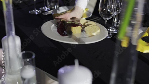 Unknown person's hand placing liver pate with sliced wheat bread and berry sauce on served table with dishes. Restaurant worker starting setting dining area with cold appetizers for special event. photo