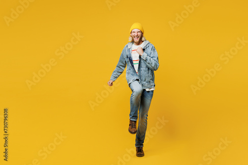 Full body young man wear denim shirt hoody beanie hat casual clothes doing winner gesture celebrate clenching fist raise up leg isolated on plain yellow background studio portrait. Lifestyle concept photo