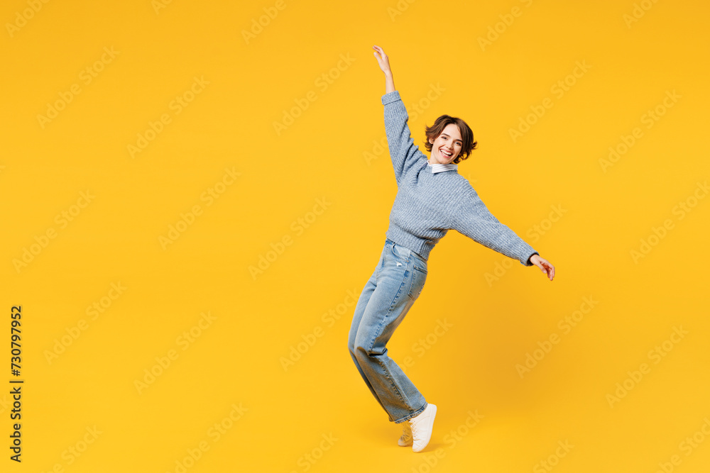 Full body side view young woman wear grey knitted sweater shirt casual clothes leaning back with outstretched hands stand on toes fooling around isolated on plain yellow background. Lifestyle concept