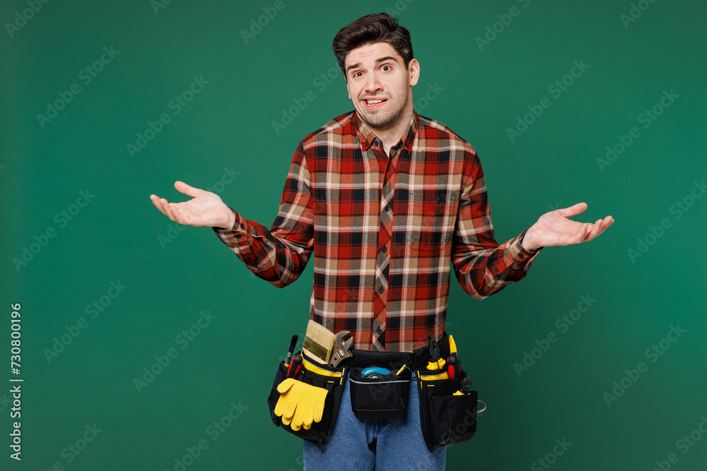 Young sad mistaken employee laborer handyman man wears red shirt spread hands say oops isolated on plain green background. Instruments accessories for renovation apartment room. Repair home concept. Young sad mistaken employee laborer handyman man wears red shirt spread hands say oops isolated on plain green background. Instruments accessories for renovation apartment room. Repair home concept.