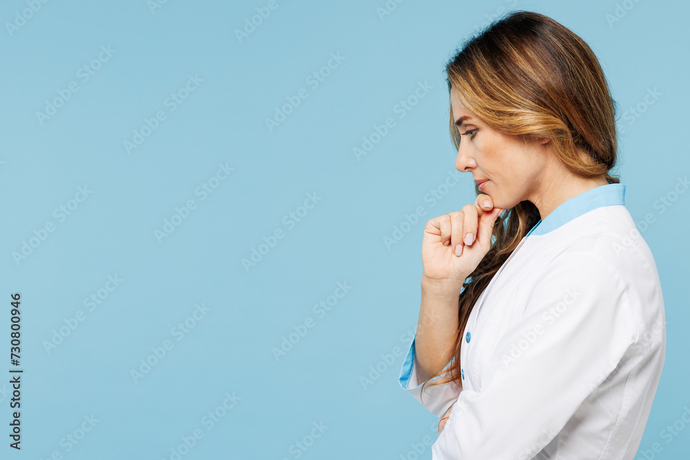 Side profile view minded thoughtful female doctor woman wear white medical gown suit work in hospital clinic office prop up chin isolated on plain blue background studio. Health care medicine concept Side profile view minded thoughtful female doctor woman wear white medical gown suit work in hospital clinic office prop up chin isolated on plain blue background studio. Health care medicine concept