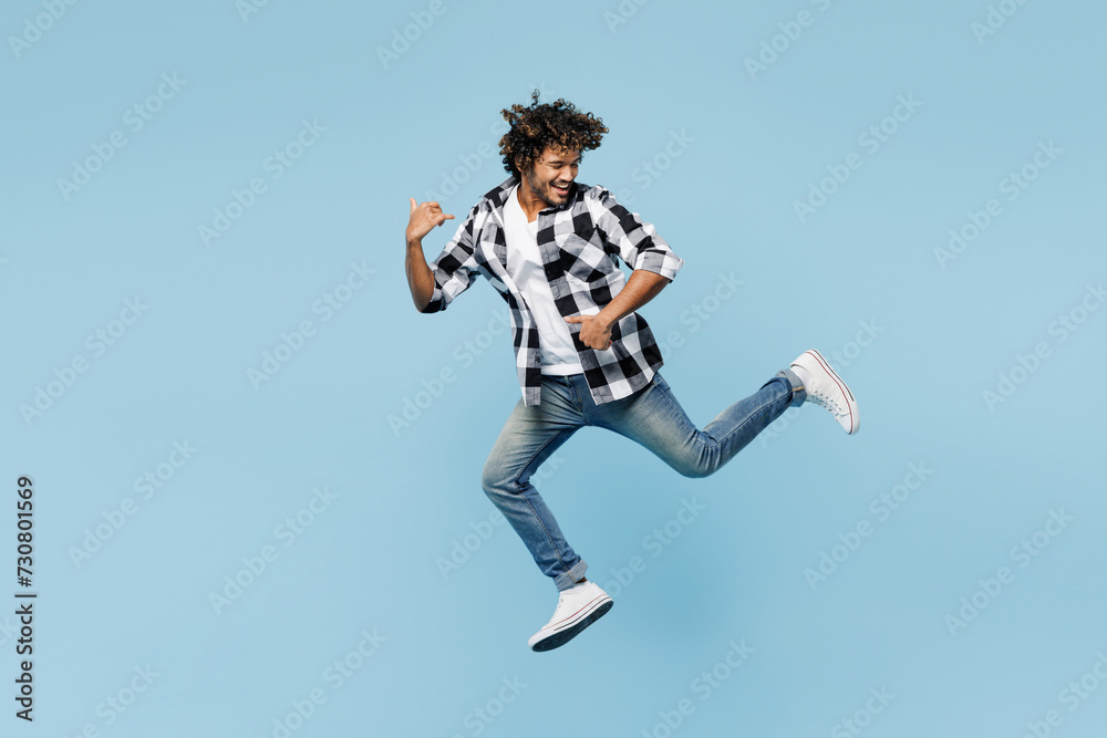 Full body side view young Indian man he wears shirt white t-shirt casual clothes jump high run fast look aside isolated on plain pastel light blue cyan background studio portrait. Lifestyle concept.