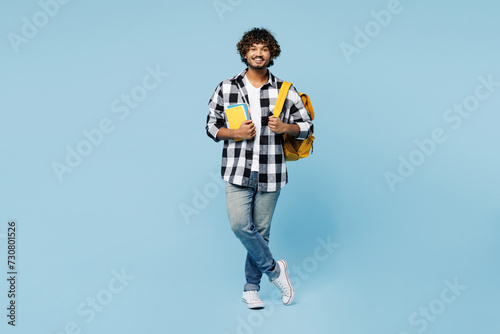 Full body smiling happy young Indian boy student wear shirt casual clothes backpack bag hold books look camera isolated on plain pastel light blue background. High school university college concept.