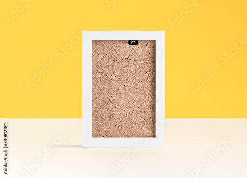 White blank photo frame on white table in front of yellow background with copy space.
